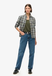 Camisa de franela a cuadros en gris y azul, camiseta sin mangas verde oscuro, jeans azules de cintura alta, zapatos negros y cinturón plateado. Presentación de un atuendo casual.
