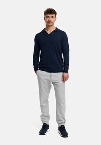Navyblaues Langarm-Polohemd mit V-Ausschnitt, kombiniert mit hellgrauen Hosen und navyblauen Sneakern, mit einer glatten Textur und tailliertem Design.