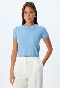 Maglione azzurro chiaro a maniche corte con scollo rotondo, impreziosito da un design di perline simili a perle sul colletto. Finitura a maglia liscia.