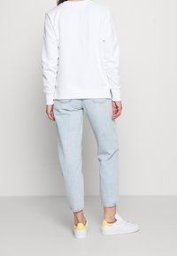 Sudadera blanca de manga larga, corte relajado, combinada con jeans de mezclilla azul claro y zapatillas blancas con detalles en amarillo.