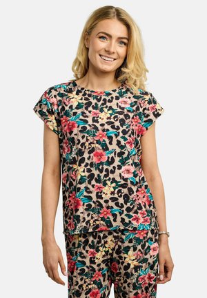 Femeie zâmbitoare cu păr blond, purtând un top și pantaloni bej asortați, cu modele negre de leopard și florale colorate.