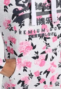 Felpa grigia con stampa floreale rosa e dettagli neri. Presenta una tasca frontale, cordini e un logo del marchio ben visibile sul petto.