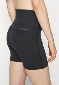 Černé šortky s vysokým pasem vyrobené z pružné látky. Mají ploché švy a logo AeroReady na zadní straně. Hladká textura.