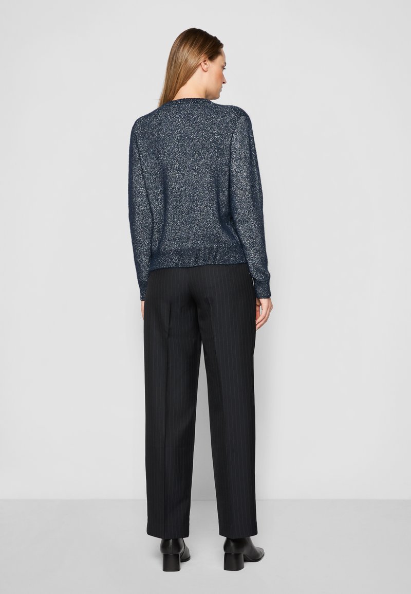 Marineblauer Glitzersweater mit bequemer Passform, rundem Ausschnitt und geripptem Saum, kombiniert mit schwarz gestreiften, hoch taillierten Hosen und Stiefeletten mit Blockabsatz.