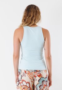Top senza maniche azzurro chiaro con un design aderente. Tessuto liscio, scollatura rotonda e dettagli arricciati sul retro. Abbinato a pantaloni con motivo floreale.