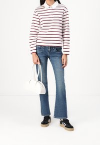 Camisa polo blanca de manga larga con rayas marrón, combinada con jeans acampanados azules y zapatillas negras. Lleva un pequeño bolso blanco.