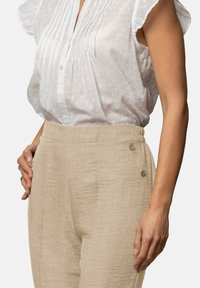 Camisa blanca de manga corta con puntos texturizados y pliegues, combinada con pantalones de lino beige que tienen dos botones en la cinturilla.
