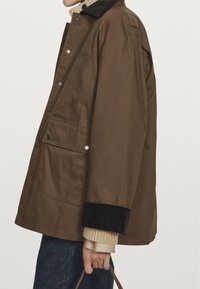 Braune Baumwolljacke mit einem Cordkragen, Druckknöpfen und zwei Fronttaschen. Die Ärmel verfügen über schwarze Cord-Details.