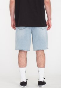Hellblaue Jeansshorts mit lockerem Schnitt, ausgestattet mit zwei Gesäßtaschen und geraden Saumabschlüssen, kombiniert mit weißen Socken und schwarzen Schuhen.
