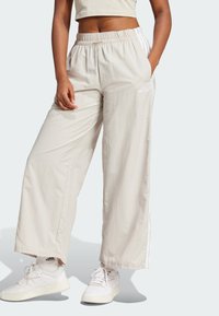 Μπεζ παντελόνια με φαρδιά γραμμή, φτιαγμένα από ελαφρύ ύφασμα, με ελαστική μέση και λευκές ρίγες στα πλάγια. Συ�νδυάζονται με λευκά αθλητικά παπούτσια.