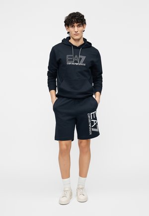 Tumesinine puuvillane kapuutsiga pusa ja lühikeste pükste komplekt, millel ees logo print. Sile tekstuur, kapuuts paelaga ja taskud lühikestel pükstel.