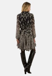 Schwarz-weiß gemustertes Kleid mit lockerem Schnitt, langen Ärmeln, tailliertem Bund und schichtartigem Rock. Trägt kniehohe schwarze Stiefel.