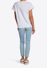 T-shirt bianco a maniche corte con risvolti, abbinato a jeans skinny azzurri chiari. Dettaglio logo discreto sul retro della maglietta. Calzature informali.
