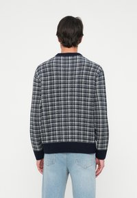 Ναυρικό και λευκό πουλόβερ πλεκτό σε καρό σχέδιο, με ριγωτό γιακά και μανίκια, διαθέτοντας υφή και χαλαρή εφαρμογή.