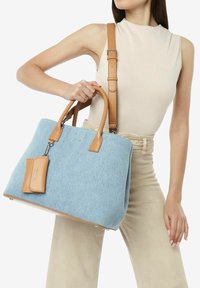 Blå filt handbag med brune læderdetaljer, struktureret form, metalbeslag og et aftageligt navneskilt. Bærehåndtag og justerbar rem.