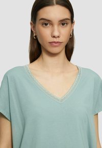 Lichtblauw katoenen V-hals top met korte mouwen, voorzien van een delicate kanten rand rond de halslijn. Zachte textuur en een relaxte pasvorm.