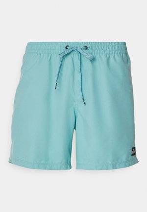 Bañador azul claro con cinturilla elástica, cordón ajustable y un pequeño logotipo negro en el lateral. Textura de tela suave.