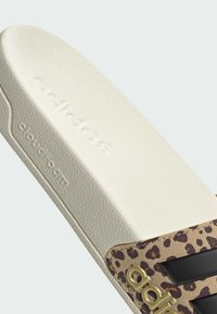 Pantofle v designu leopardího vzoru se světlou texturovanou pěnovou stélkou, s černými detaily a zlatým logem. Navrženy pro pohodlí a každodenní nošení.