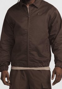 Brown zip-front jacket made of smooth fabric, featuring elastic cuffs and a discreet logo on the chest. Regular fit and classic collar design.