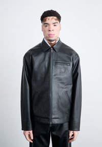 Veste en cuir noir avec fermeture éclair sur le devant, col pointu et petite poche poitrine. Comprend des poches latérales et une texture lisse.
