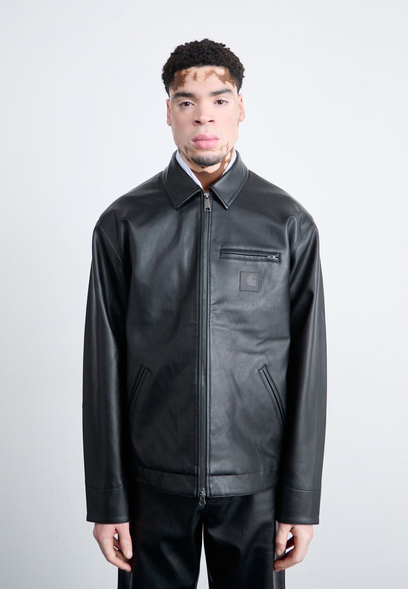 Veste en cuir noir avec fermeture éclair sur le devant, col pointu et petite poche poitrine. Comprend des poches latérales et une texture lisse.
