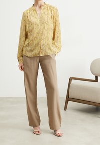 Yellow patterned blouse with a stand collar, paired with light brown wide-leg trousers. Smooth texture; blouse features buttoned front, long sleeves.