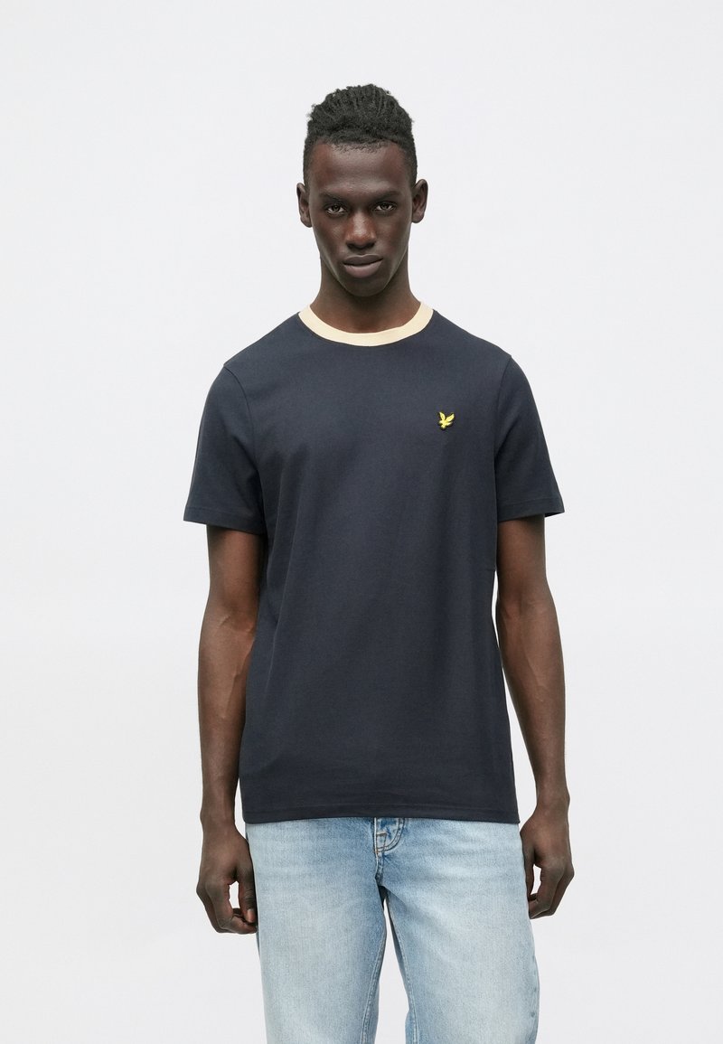 Sötétkék pamut póló világos bézs kerek nyakkivágással és egy kis sárga hímzett logóval a mellkason. Rövid ujjú, klasszikus fazon.