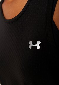 Camiseta deportiva negra sin mangas con un patrón texturizado, que presenta un logo plateado de Under Armour en el área izquierda del pecho. Tela suave, cuello redondo.
