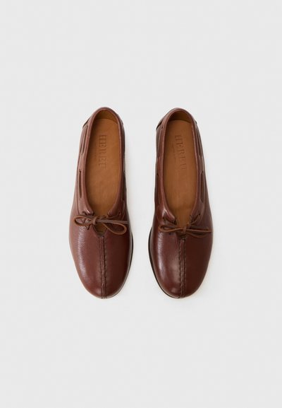 Zapatos de cuero marrón tipo mocasín con punta redondeada, detalle de costura y cierre con cordones. Textura suave y diseño minimalista.