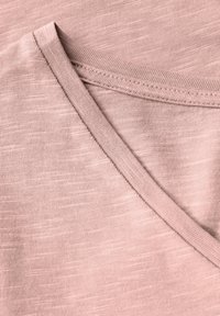 Tessuto rosa con una sottile trama. Scollatura a V con un bordo a contrasto, caratterizzata da cuciture lisce e un aspetto leggero.