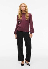 Pull en maille bordeaux avec des manches longues et bouffantes, associé à un pantalon noir à jambes droites et des escarpins noirs pointus. Texture lisse et design décontracté.