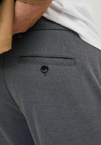 Graue Hose aus strukturiertem Stoff, mit einer Gesäßtasche und einem schwarzen Knopf sowie einem taillierten Bund.