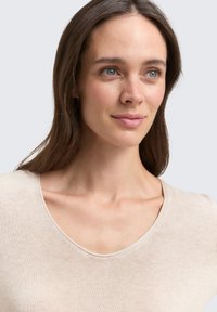 Beige V-veida krekls, izgatavots no mīksta, viegla auduma. Tam ir gluda tekstūra un brīva piegriezuma forma. Kakla izgriezums uzsver minimālistisku dizainu.