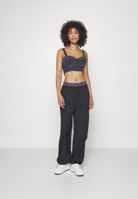 Dżinsowy crop top z grubymi ramiączkami i usztywnioną miseczką, połączony z luźnymi czarnymi spodniami bawełnianymi i białymi trampkami z czarną podeszwą.