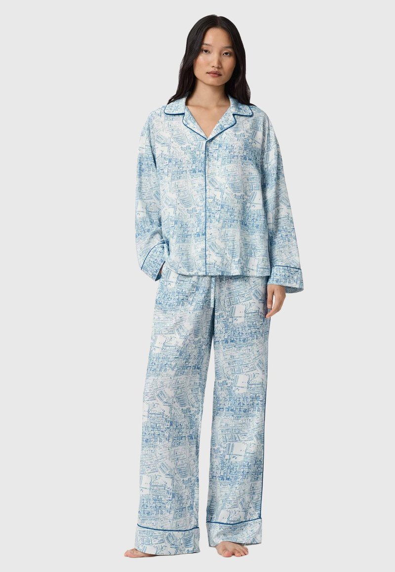 Sinivalkoinen kuviollinen pyjama-asuste, joka on valmistettu pehmeästä kankaasta. Rentomallinen paita, jossa on kaulus, sekä yhteensopivat housut, joissa on joustava vyötärö ja kuminauha lahkeissa.