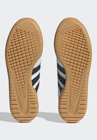 Baskets blanches avec des rayures noires sur le dessus. Semelle en caoutchouc texturé de couleur beige, avec un motif en losange pour une meilleure adhérence.