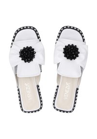 Witte instapschoenen met een grote zwarte geborduurde bloemenaccent, een bovenwerk van glad leer, vierkante neus en decoratieve zwart-wit rand.