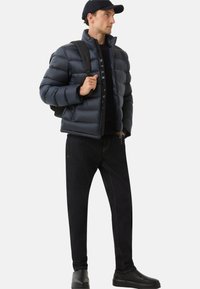 Námořnická péřová bunda s vysokým límcem, prošívaný design, zapínání na zip, nošena přes černou mikinu, v kombinaci s tmavými džíny a černými botami.