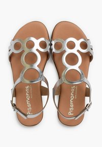 Sandali metallici argento con ritagli circolari, soletta in pelle marrone, cinturino alla caviglia con fibbia, suola piatta, design minimalista.