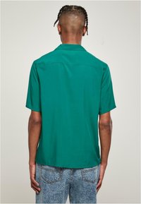 Korte mouwen shirt van effen groene stof, met een relaxte kraag, een gladde textuur en een rechte zoom, gecombineerd met lichtblauwe, getextureerde jeans.