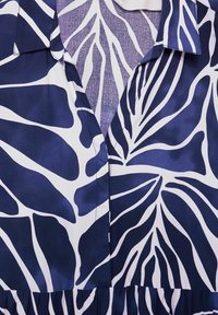 Mörkblått och vitt mönstrat tyg med lövmotiv, med en knapp-up krage och ett gatherat nederkant, tillverkat i ett lätt, jämnt material.