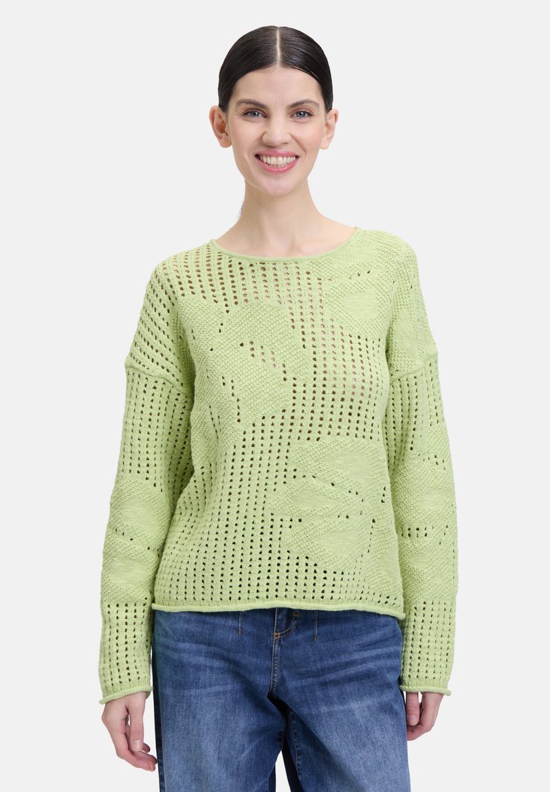 Pull en maille vert clair avec une coupe ample, présentant des motifs en tissages ouverts et des manches longues. Le tissu texturé ajoute de la profondeur au design.