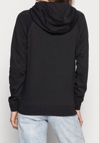 Svart hoodie med dragsko på huvan, raglanärmar, ribbad nederkant och muddar, tillverkad av mjukt tyg, som bärs över ljusblå jeans.