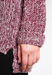 Gestrickter Pullover in Burgunderrot und Creme mit strukturiertem Muster, der mit breiten Bündchen und Seitenschlitzen für eine lockere Passform ausgestattet ist.