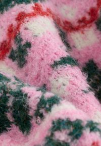 Pletená deka s textúrovaným vzorom v ružovej, zelenej a bielej farbe. Materiál vyzerá nadýchane s jemným, útulným povrchom.