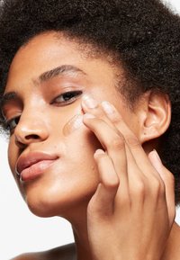 Crema idratante per il viso applicata sulla pelle, di consistenza cremosa e colore marrone chiaro. Il modello ha un incarnato medio e capelli corti e texturizzati.