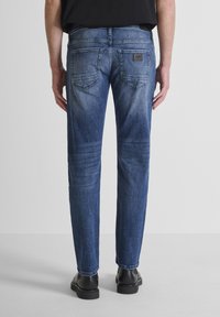 Vaqueros de denim azul oscuro con corte recto, que presentan un parche de cuero en la parte posterior, dos bolsillos traseros y un ligero desgastado en los muslos.
