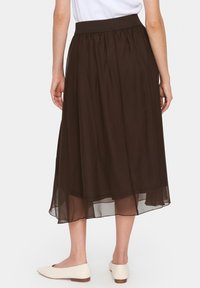 Gonna midi marrone fluente con sovrapposizione trasparente, vita elastica e texture arricciata. Abbinata a mocassini chiari e appuntiti.