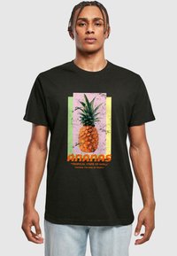 Fekete póló ananász grafikával, texturált elemekkel. A szöveg tartalmazza az "ANANAS" feliratot és egy szlogent, pasztell színblokkok hátterében.
