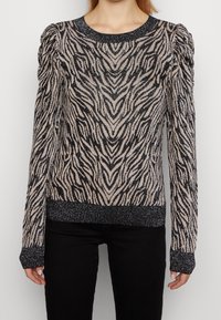 Maglione aderente a maniche lunghe con stampa zebra nera e beige, polsini, orlo e colletto neri brillanti, indossato con pantaloni neri.